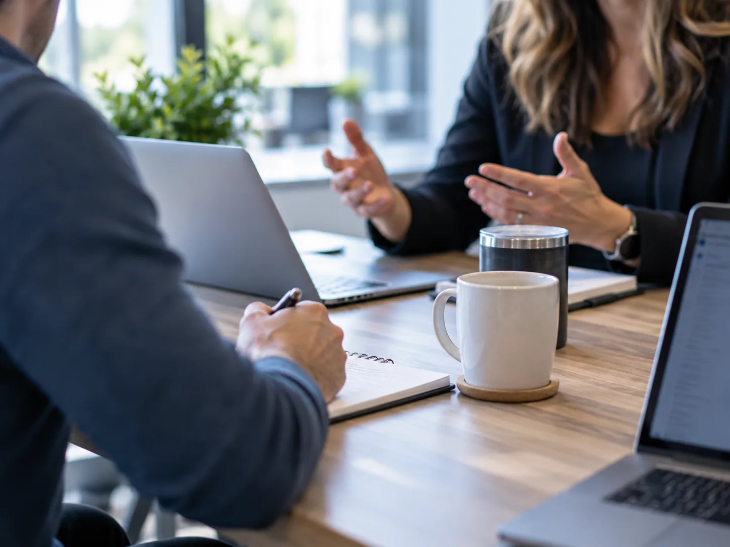 Two colleagues in conversation at a table with laptops